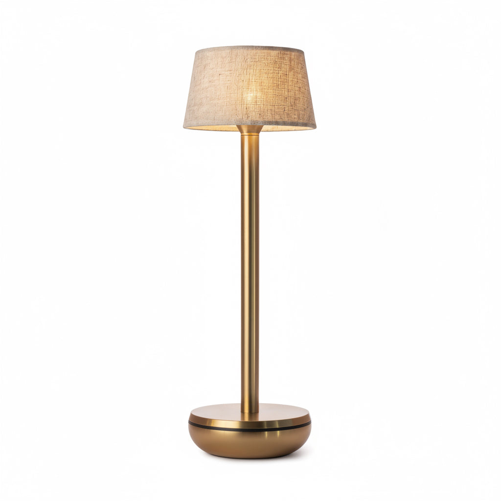 A modern table lamp with a warm brass-finished metal stand and a textured beige fabric drum shade, shown illuminated against a plain white background.