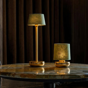 Two table lamps on a round wooden table with dark curtains in the background