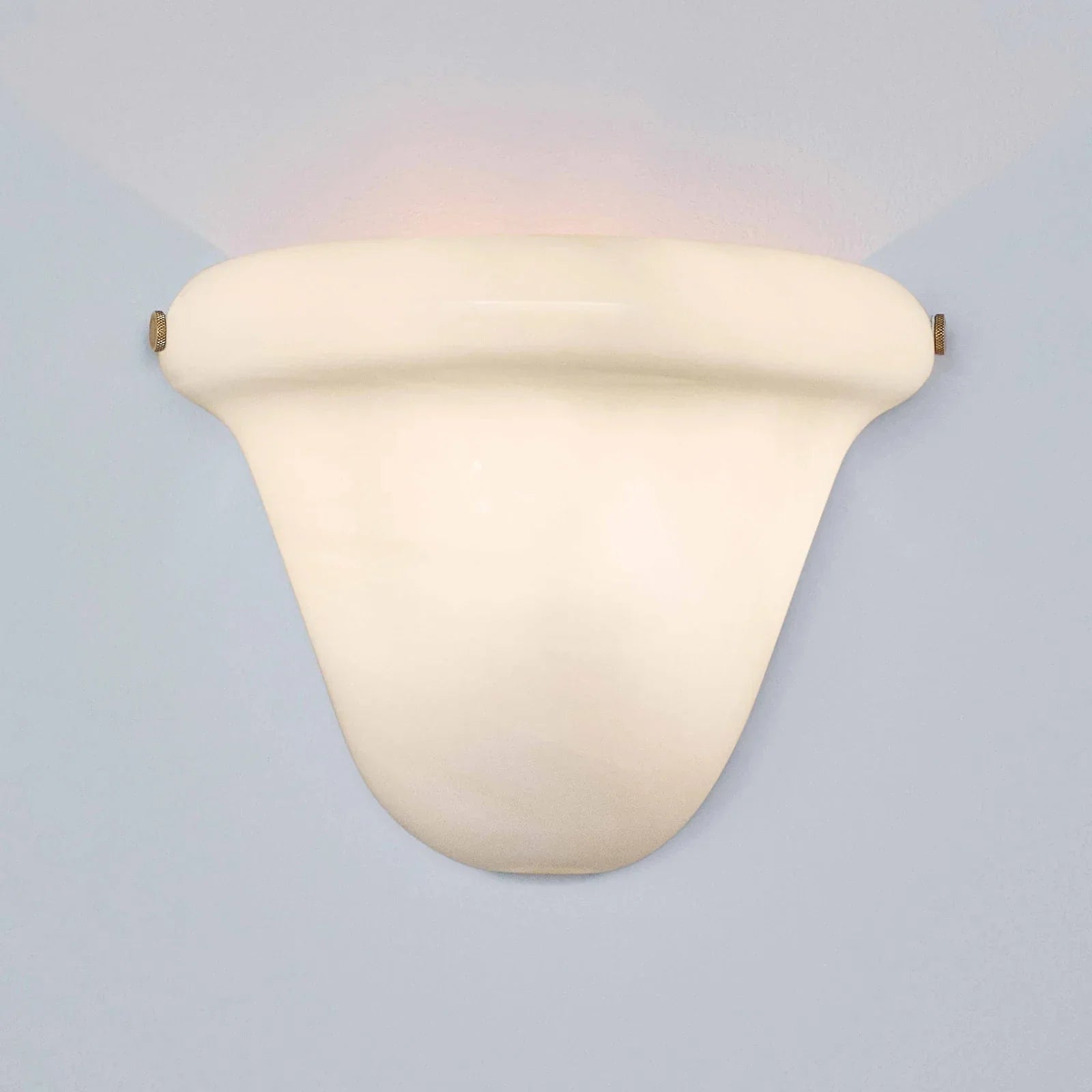 A modern wall-mounted sconce with a curved, shield-like shade in a warm cream or off-white finish, casting a soft warm light upward and downward against a pale blue-gray background.