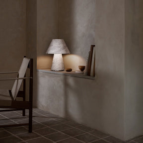 Lamp on a shelf in a dimly lit room with textured walls and tiled floor.