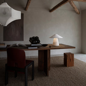 Modern interior with wooden desk, chair, and lamp in a room with exposed beams.