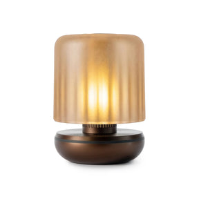 A modern table lamp with a ribbed, translucent amber-tinted glass shade and a dark bronze metallic base, shown illuminated against a white background.