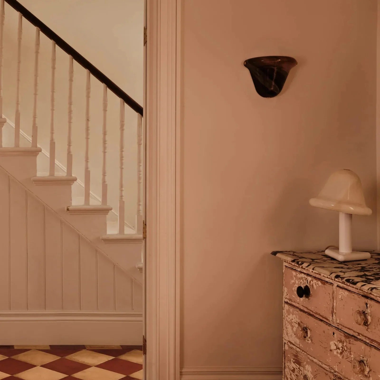 Staircase with a checkered floor and a dresser with a lamp in a room.