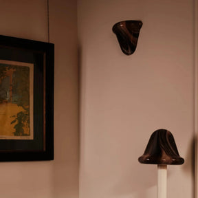 A black and cream striped armchair in a dimly lit room, next to a white floor lamp with a dark bell-shaped shade and a framed picture on the wall.